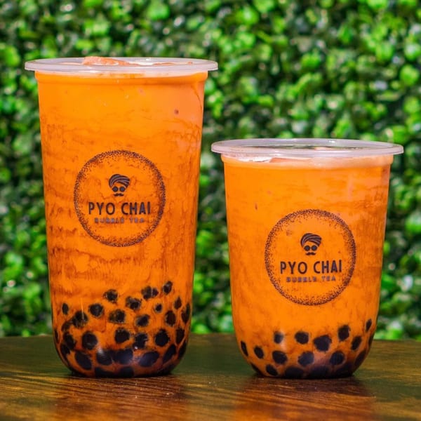 Two PYO Chai boba drinks, one large and one small, filled with orange liquid and dark boba pearls.