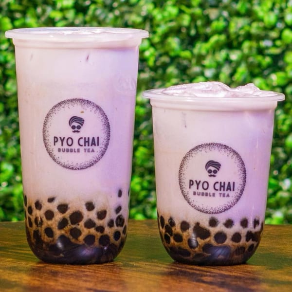 Two PYO Chai taro bubble teas with dark boba pearls, one large and one small, on a wooden surface.