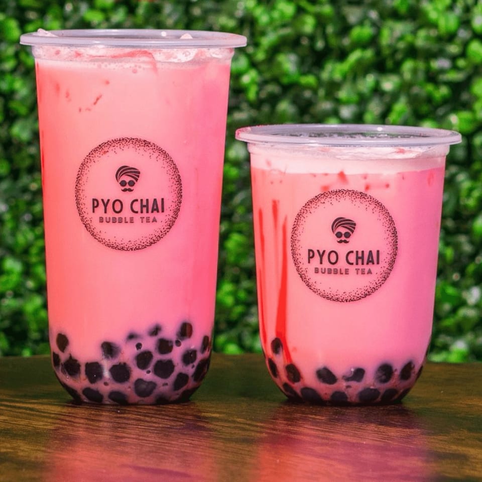 Two PYO Chai strawberry boba drinks with black tapioca pearls on a wooden table.