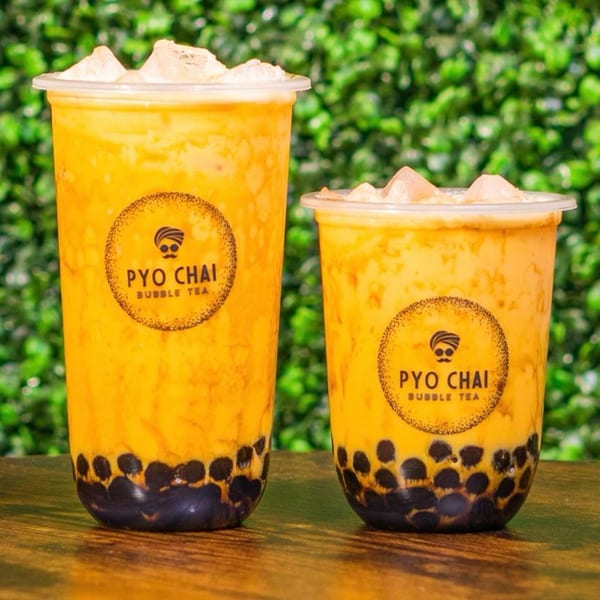 Two PYO Chai boba drinks, one large and one small, on a wooden table with a green background.