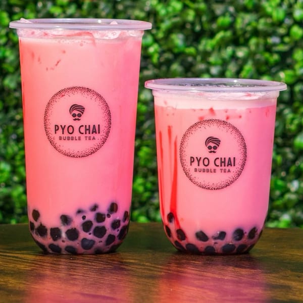 Two PYO Chai strawberry boba drinks with black tapioca pearls against a green leafy background.