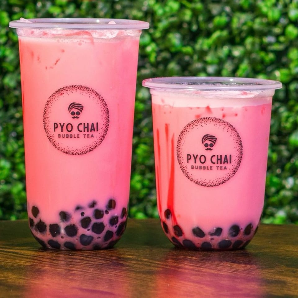 Two PYO Chai strawberry boba drinks with black tapioca pearls against a green leafy background.