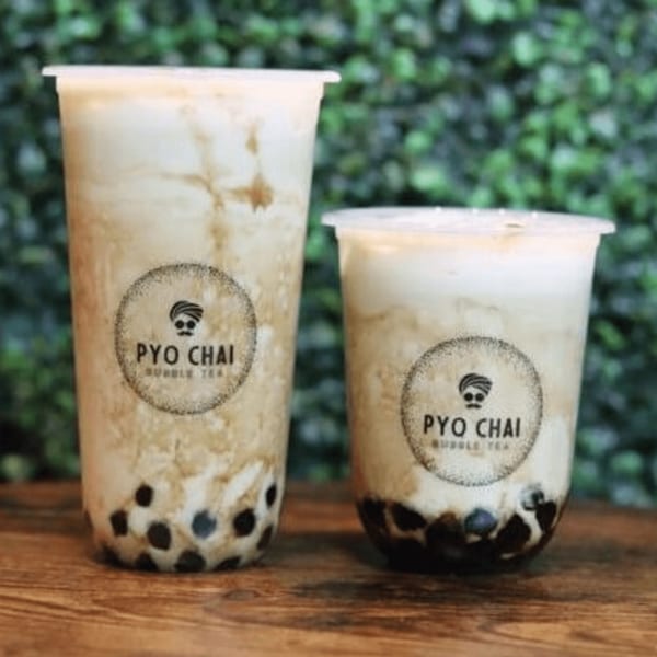 Two PYO CHAI bubble teas, one large and one small, with tapioca pearls on a wooden surface.