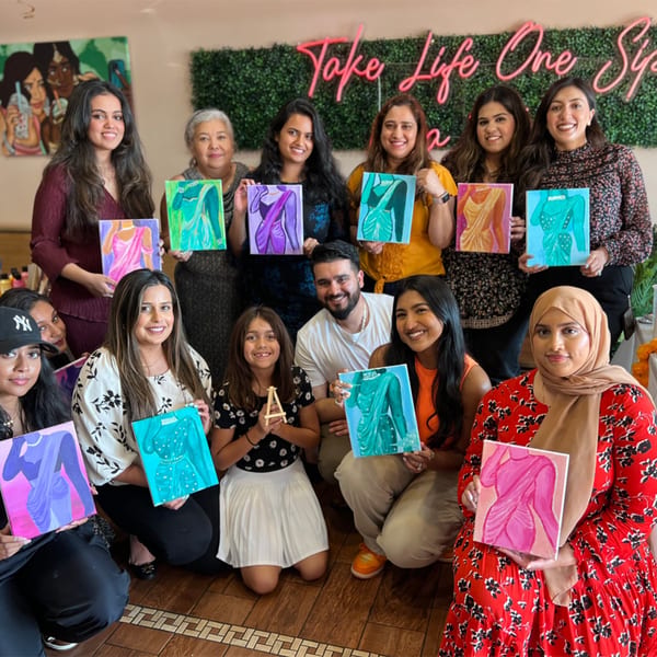 Diverse group of people smiling and holding up colorful paintings of saris at PYO Chai.