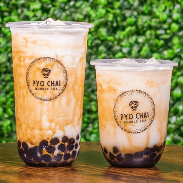 Two PYO Chai bubble teas with dark boba, creamy milk, and ice, against a green leafy background.