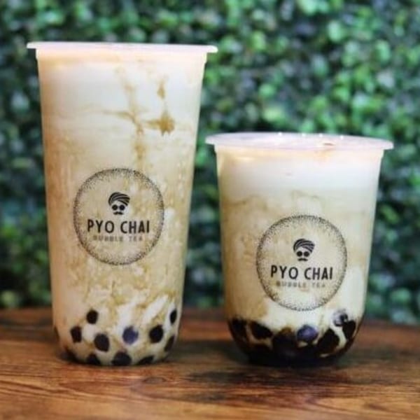 Two PYO Chai boba drinks, one large and one small, with tapioca pearls on a wooden surface.