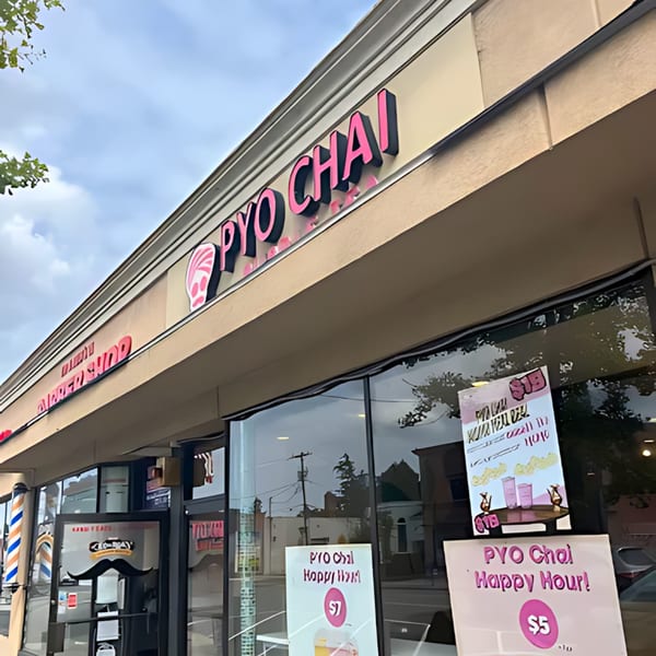 The exterior of PYO Chai boba shop with pink signage and Happy Hour specials displayed in the window.