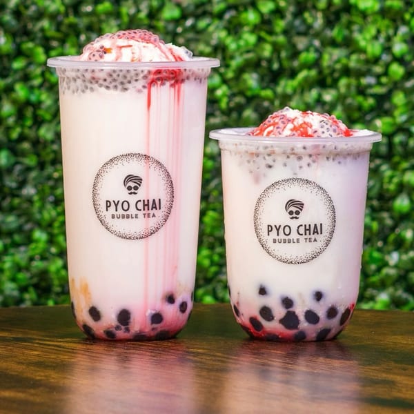 Two PYO CHAI boba drinks with white milk, black tapioca pearls, and red syrup on a wooden table.