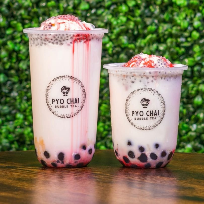 Two PYO CHAI boba drinks with white milk, black tapioca pearls, and red syrup on a wooden table.