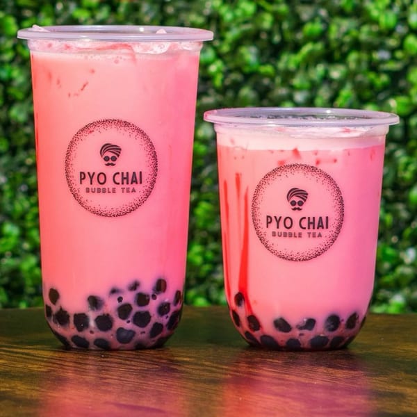 Two PYO Chai pink boba drinks with black tapioca pearls on a wooden table against a green wall.