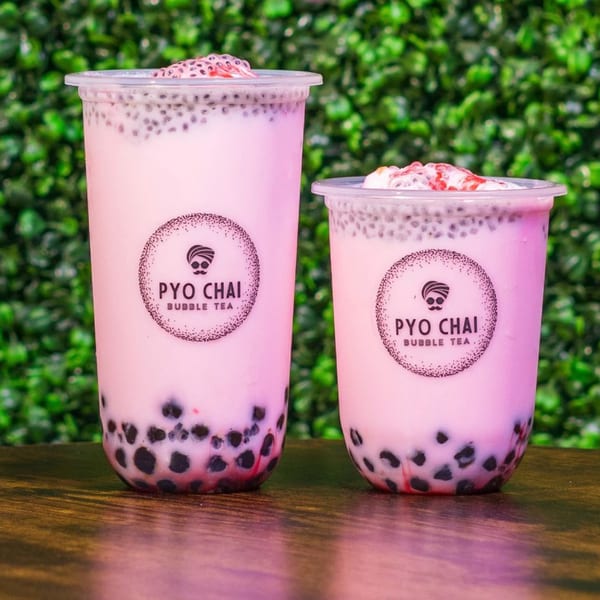 Two PYO Chai strawberry boba drinks with chia seeds and tapioca pearls on a wooden table.