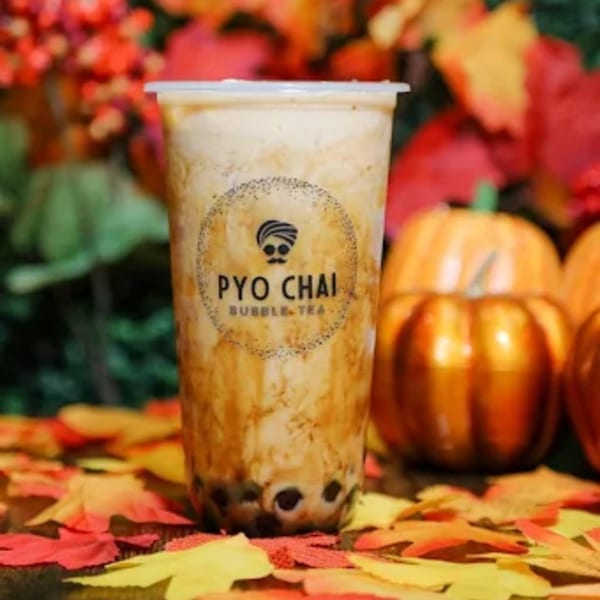 PYO Chai boba tea with dark pearls, surrounded by autumn leaves and small pumpkins.