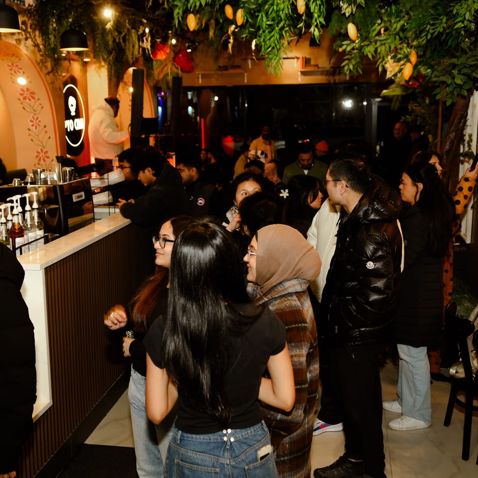 Customers gather at the counter of PYO Chai, a boba tea shop, under warm lighting and lush decor.