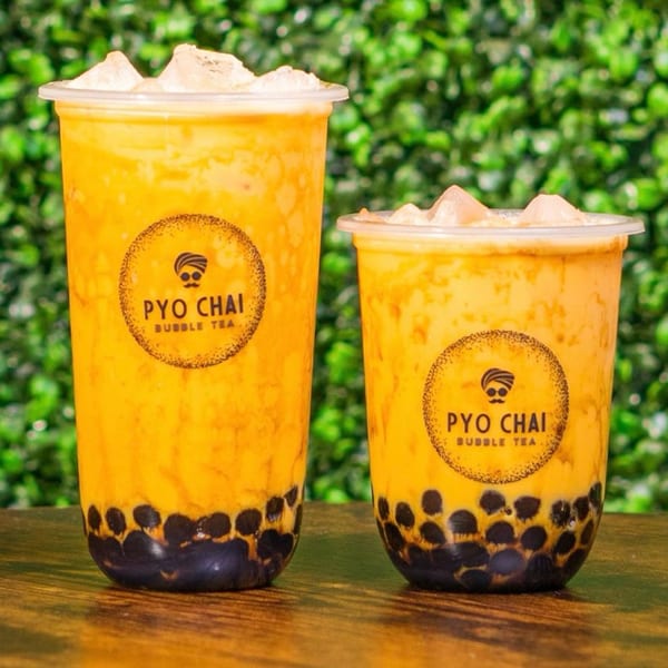 Two PYO Chai bubble teas with ice and dark boba pearls, against a green leafy background.