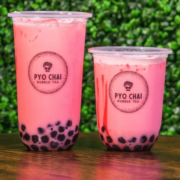 Two PYO Chai strawberry boba drinks with black tapioca pearls on a wooden table.