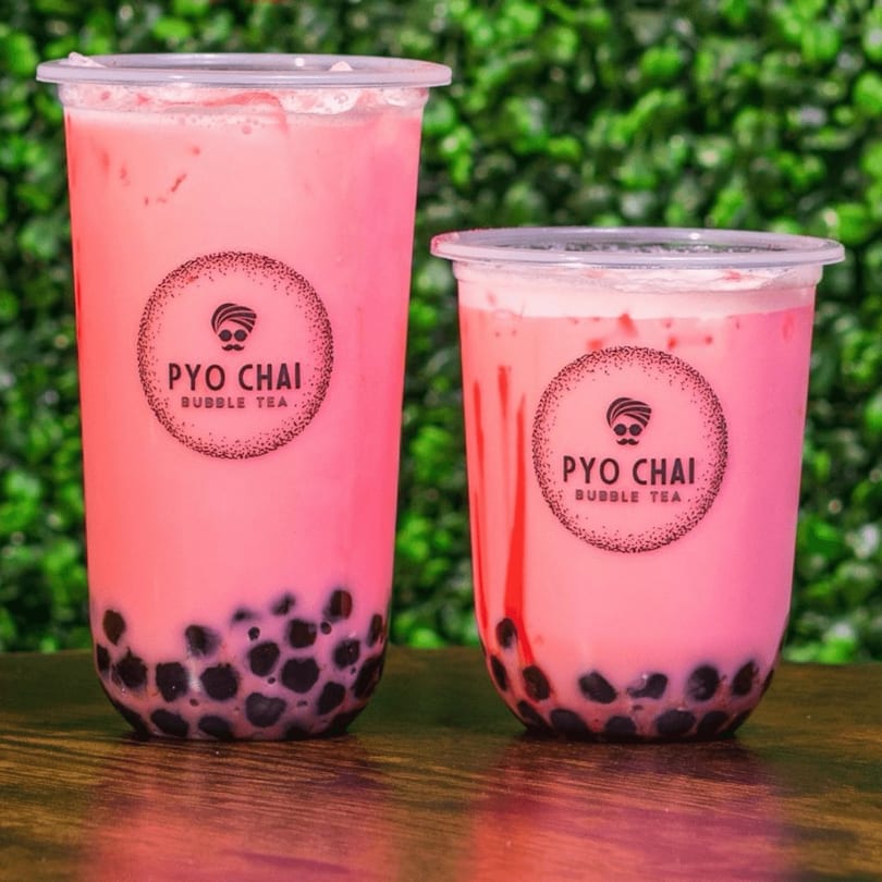 Two PYO Chai strawberry boba drinks with black tapioca pearls on a wooden table.