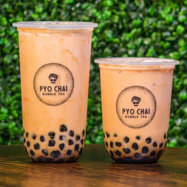 Two PYO Chai bubble tea drinks, one large and one small, on a wooden surface.