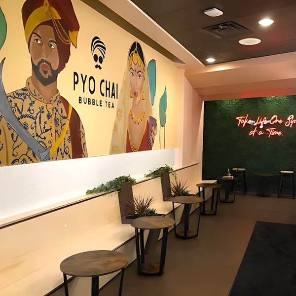 PYO Chai bubble tea shop interior with a large mural, small tables, and a neon sign.