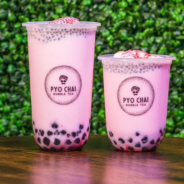 Two PYO Chai strawberry boba drinks with chia seeds and fruit, on a wooden table.